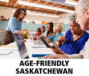 Thumbnail image of younger woman teaching a computer class to a smiling, diverse group of older adults. Caption is Age-Friendly Saskatchewan.
