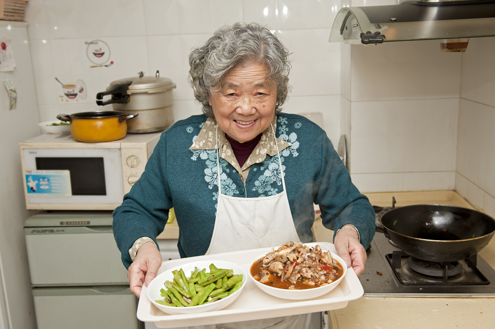 Image of smiling older Asian woman showing the meal she has just cooked.