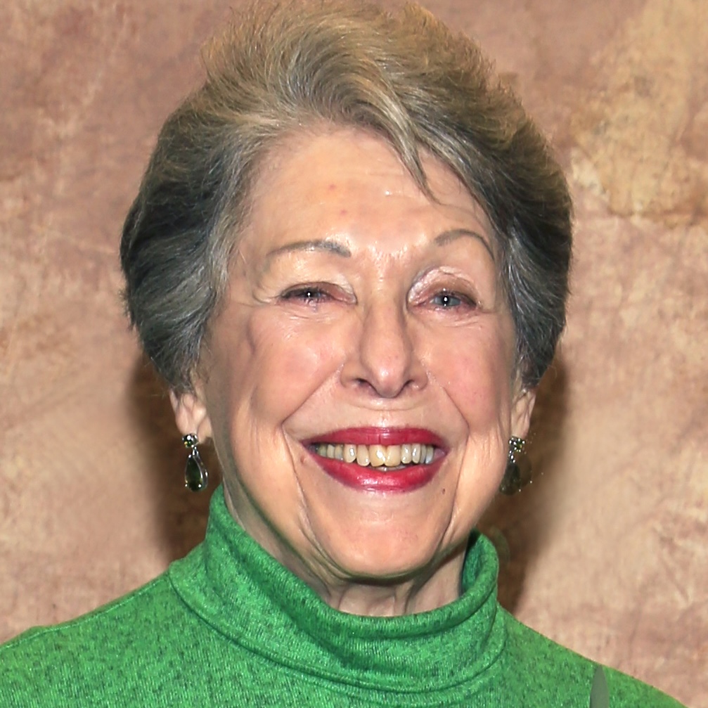 Thumbnail headshot of Lyn Goldman. Smiling older woman with graying hair, wearing green.